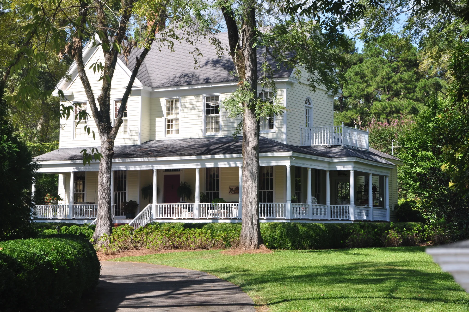One-story stuccoed brick Jerry Cowles Cottage behind a shaded front lawn